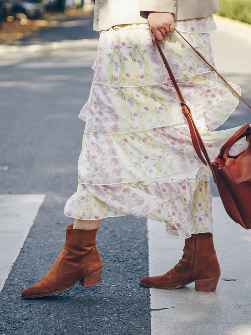 Person wearing a floral skirt and brown boots on a street.